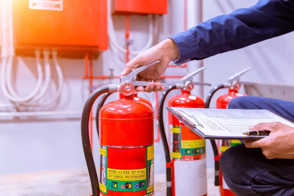 midsection worker examining fire extinguishers with checklist pen factory